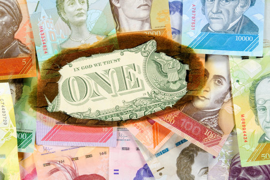 Concept of hyperinflation in Venezuela. Burned Venezuelan money with the image of statesmen, through hole in which you can see an unburned one dollar bill. Close up.