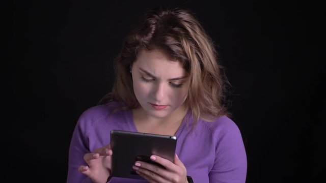 Portrait of woman working with tablet with perplexity on black background.
