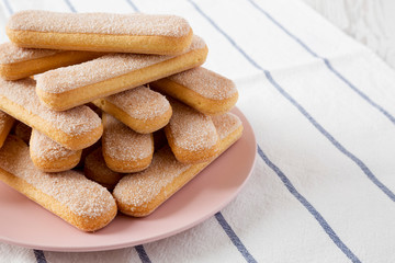 Savoiardi or ladyfingers cookies on pink plate on cloth, low angle view. Close-up. Copy space.