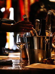 Fototapeta na wymiar wine tasting: there is a glass of wine on a wooden table, and a silver bucket for cooling wines with open bottles of champagne, from which a bottle is taken out.