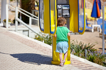 Small child on a hot summer day in the telephone booth on the beach waiting for a call - 262090904