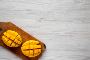 Sweet mangoes on rustic wooden board over white wooden surface, top view. Flat lay, from above, overhead. Copy space.