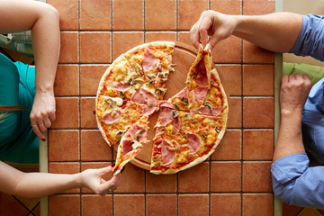 delicious pizza with mushrooms, cheese and sausage, cut into eight pieces, two of which are held in the right hands of a man and a woman - 262091109
