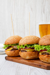 Homemade cheeseburgers and glass of beer on a white wooden surface, side view. Close-up.