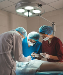 Group of surgeons at work operating in surgical theatre. Resuscitation medicine team wearing protective masks holding steel medical tools saving patient. Surgery and emergency concept.