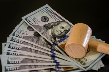 One hundred dollar bills and a wooden hammer against a black background. Close-up.