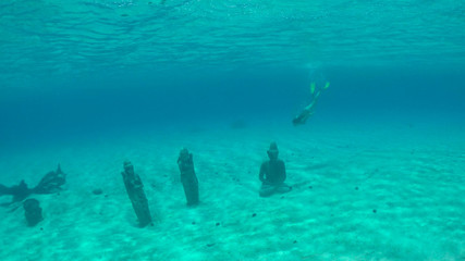 Fototapeta na wymiar UNDERWATER: Woman on vacation diving and exploring ruins of old buddha statues.