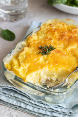 Potato casserole with fish and cheese on a light grey background.