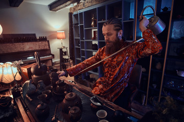 Fototapeta na wymiar Chinese tea ceremony. Caucasian master in kimono making natural tea in the dark room with a wooden interior, using a teapot with a long spout. Tradition, health, harmony. Chinese tea ceremony