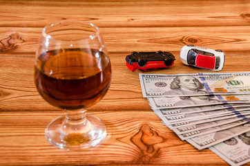 a glass of wine, dollars and toy cars on a wooden background.
