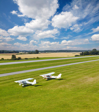 two white pleasure planes on a bright sunny day on the runway of the airfield from a bird's flight in the background of the field