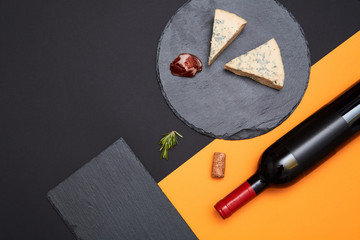 Layout of blue cheese with prosciutto slices on black slate board with bottle of wine on colorful...