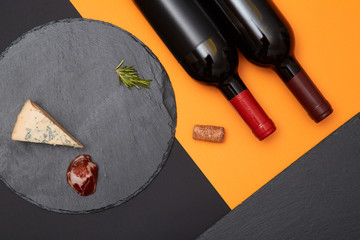 Composition of blue cheese with prosciutto slices on black slate board with bottle of wine on...