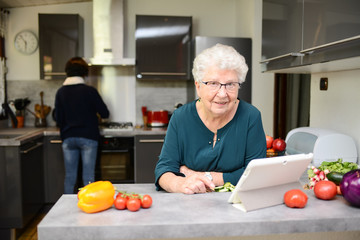 happy senior active woman cooking at home in modern kitchen and looking for recipe on a internet computer tablet