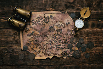 Old map, compass and binoculars on a adventurer table background. Treasure hunt concept.