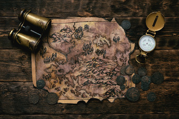 Old map, compass and binoculars on a adventurer table background. Treasure hunt concept.