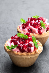 Mini tarts with pink cream and pomegranate seeds on black stone background