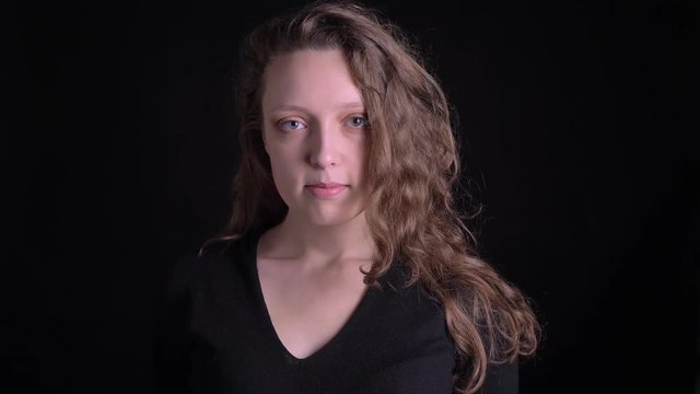 Portrait of young curly-haired girl watching awkwardly into camera on black background.