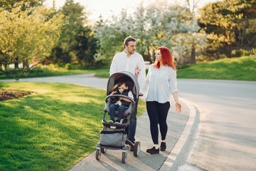beautiful and stylish redhead mom in a white blouse wallking with her beautiful man dressed in a white shirt and blue jeans and they carry their little son in a cart