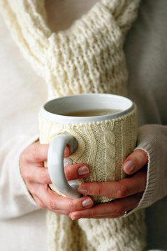 Woman's hands holding a mug in knit cozy