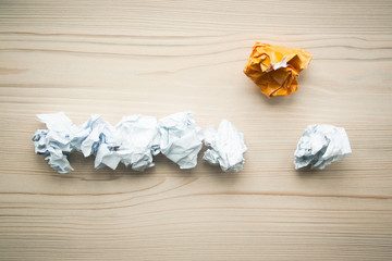 Line of crumpled white paper balls with one different orange paper ball above them. Concept of think different, think out of the box, leadership.