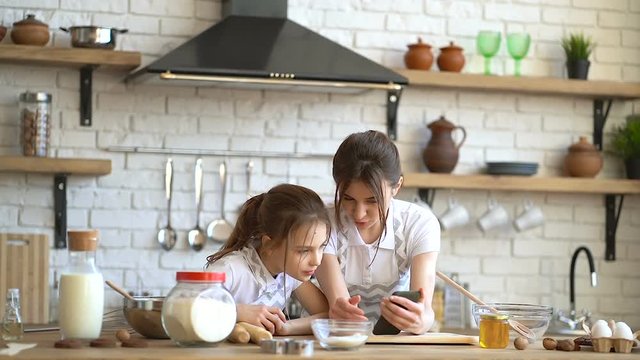 Two sisters looking recipe at the smartphone and cheking ingredients before cooking. 