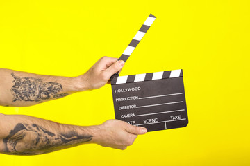 director's clapper. hands with a boardсlapper on a yellow background.