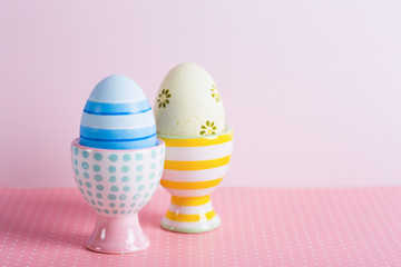 Closeup two colorful painted Easter eggs in vibrant modern egg stands on pastel pink background.