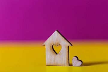 Obraz na płótnie Canvas Closeup wooden house with hole in form of heart on vibrant crimson and yellow background.