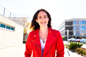 Millennial woman, with red jacket and long hair, walking and smiling sure of herself.