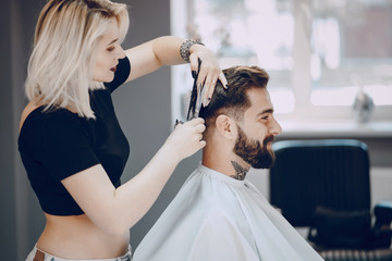 handsome young bearded guy sitting in an armchair in a beauty salon and the girl near him cuts his hair