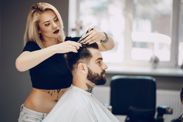 handsome young bearded guy sitting in an armchair in a beauty salon and the girl near him cuts his hair