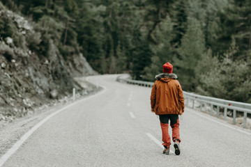 a young man with an outdoor dress and a road passing through the pine forest