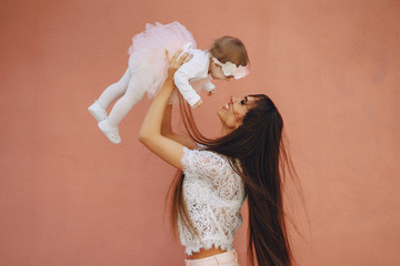 Young and very beautiful slim mum with long hair walking in a sunny summer city with her little...