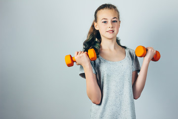Beautiful caucasian teen girl doing exercises with dumbbells.  Gray studio background, copy space. Fitness and healthy sports lifestyle.