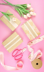 Gifts wrapped in kraft paper and pink ribbons overhead flat lay for Mother's Day, birthday or Valentine's Day celebrations.