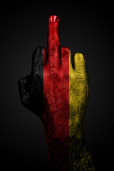 A hand with a painted flag of Germany shows the middle finger, a sign of aggression, against a dark background.