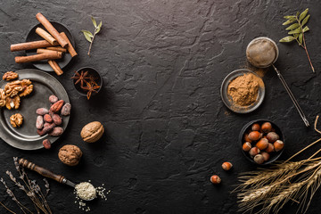Mix of nuts and spices for baking cakes in bowl and spoon, cinnamon, star anise, hazelnuts, walnuts, wheat, lavender on dark stone table. Organic food, top view, space for text