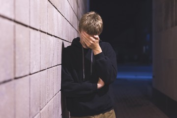 Upset teenager leaning against a brick wall in an alleyway. He is suffering from depression.