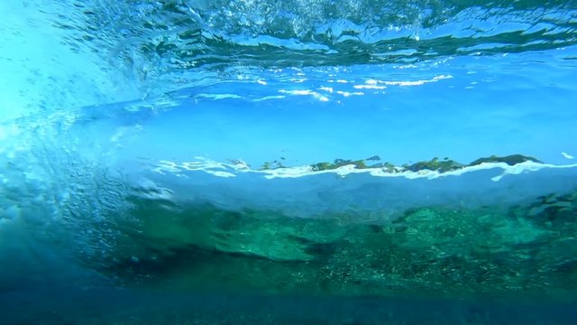Underwater view of the tropical crystal clear brekaing wave working like a big lens and refracting the coast view
