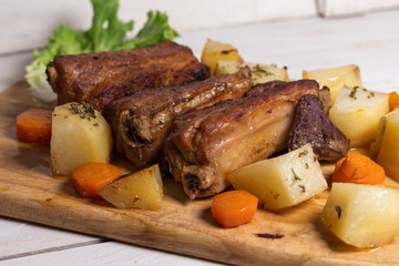 Roasted pork ribs with thyme potatoes over white wooden background, Eastern cuisine