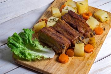 Roasted pork ribs with thyme potatoes over white wooden background, Eastern cuisine