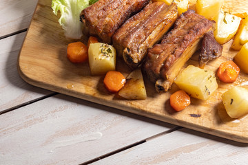 Roasted pork ribs with thyme potatoes over white wooden background, Eastern cuisine