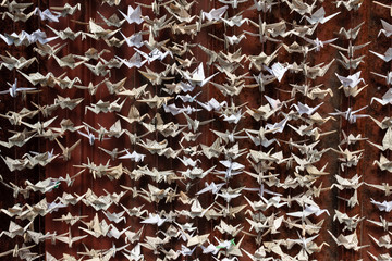 Wide detail of 1000 origami folded paper cranes sculpture against a deep red background, horizontal aspect
