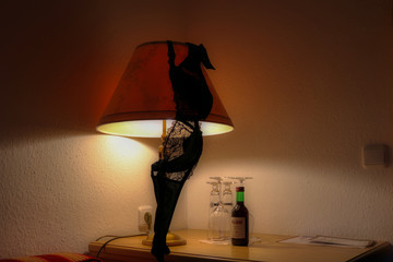 Dieses einzigartige Bild zeigt einen schwarzen BH über einer Lampe und davor eine kleine Flasche Rotwein. Dieses Bild wurde in einem Hotel in Bayern Deutschland aufgenommen
