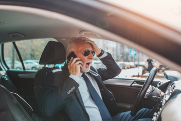 Naklejka premium Nervous senior good looking businessman getting angry and nervous while talking on mobile phone and driving his car.