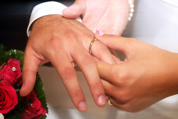 Bride's hand puts the wedding ring in the groom's finger