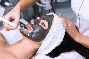 Beautiful woman receiving facial mask with rejuvenating effects in spa beauty salon.