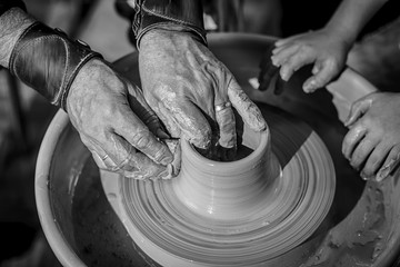 A close-up of the hand of a male potter who teaches his pupil, a child of the art of making a pot or a vase of clay. People working on potters.