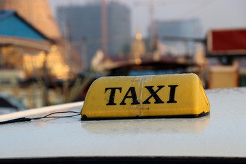 Taxi light sign or cab sign in yellow color with black text and tied with transparent tape on the car roof at the street blurred background.